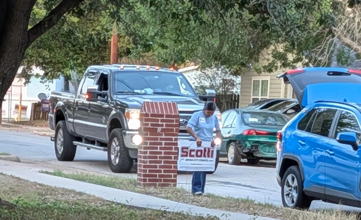 A person placing a Chris Scotti campaign sign beside a residential street.